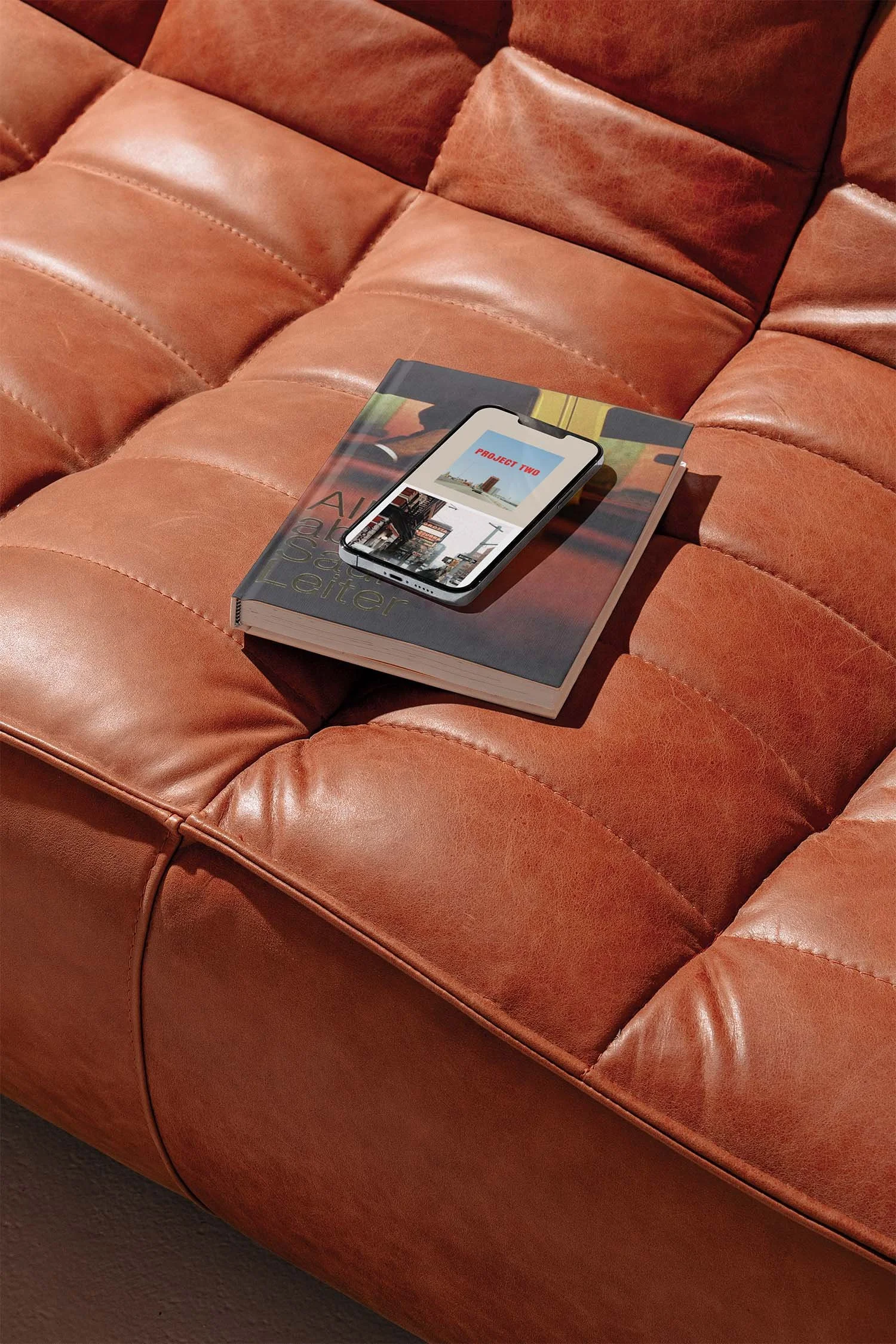 A smartphone displaying a photography portfolio layout resting on a book placed on a brown leather sofa, illustrating a mobile-friendly Squarespace website design for photographers.