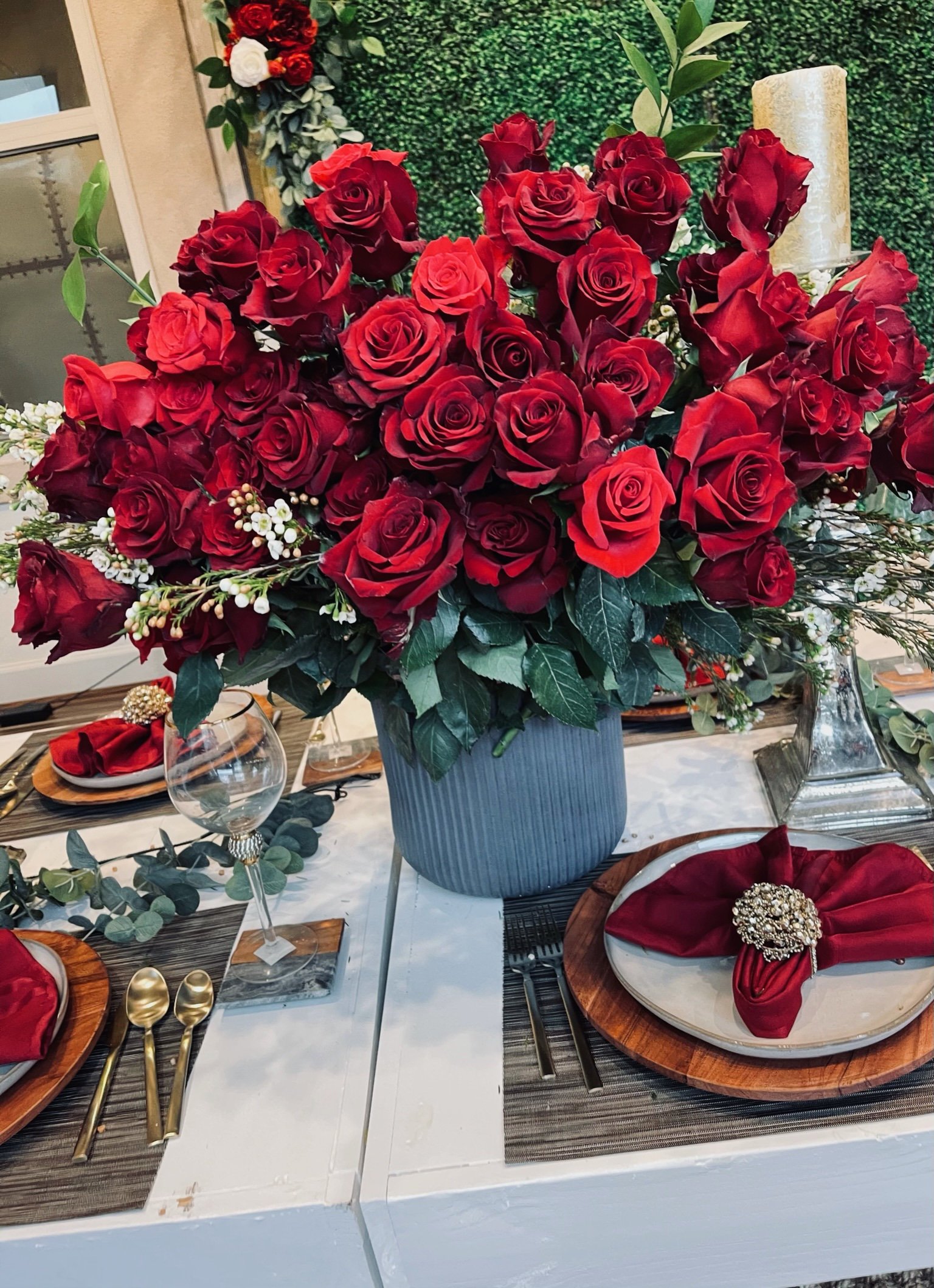 A table centerpiece with a large bouquet of red roses in a blue vase, decorated for a formal event.