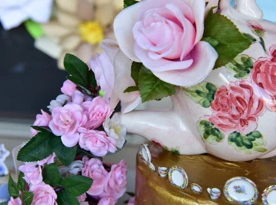 Decorative porcelain teapot with pink roses and green leaves, placed on a gold-colored surface with small decorative mirrors.