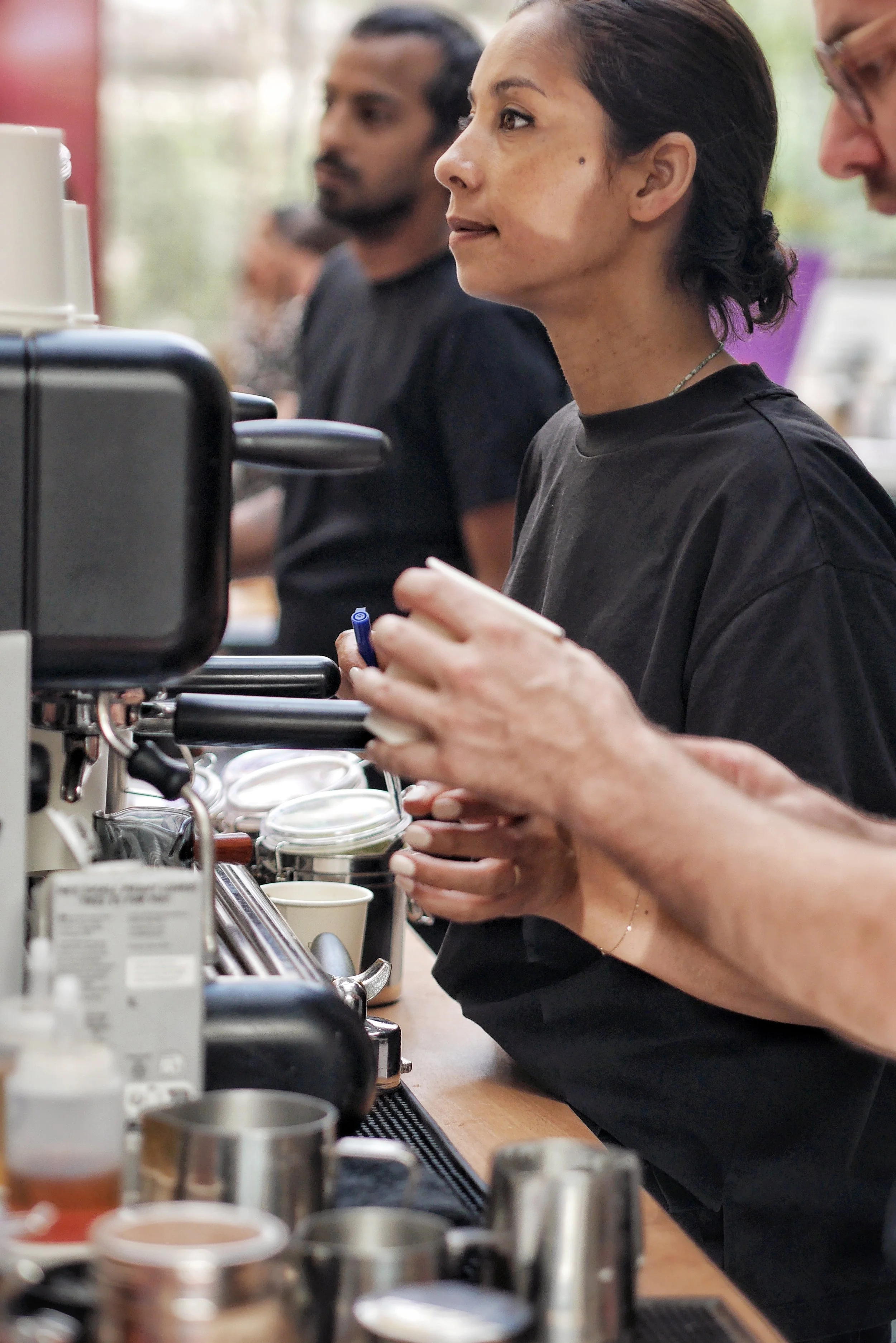 Une femme en train de préparer une boisson dans un café, entourée de personnes et d'équipements de barista.