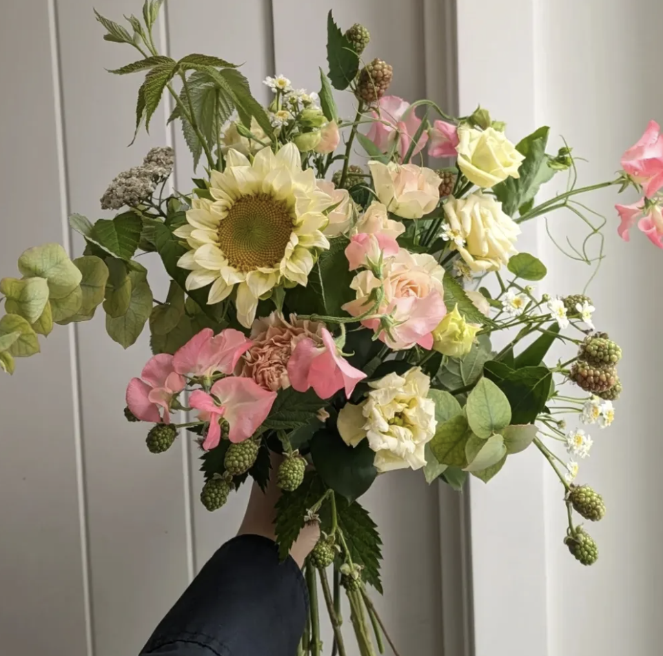 Un bouquet mélangé de fleurs, notamment un tournesol, des roses jaunes et roses, des hortensias roses, et d'autres fleurs et feuillages verts.