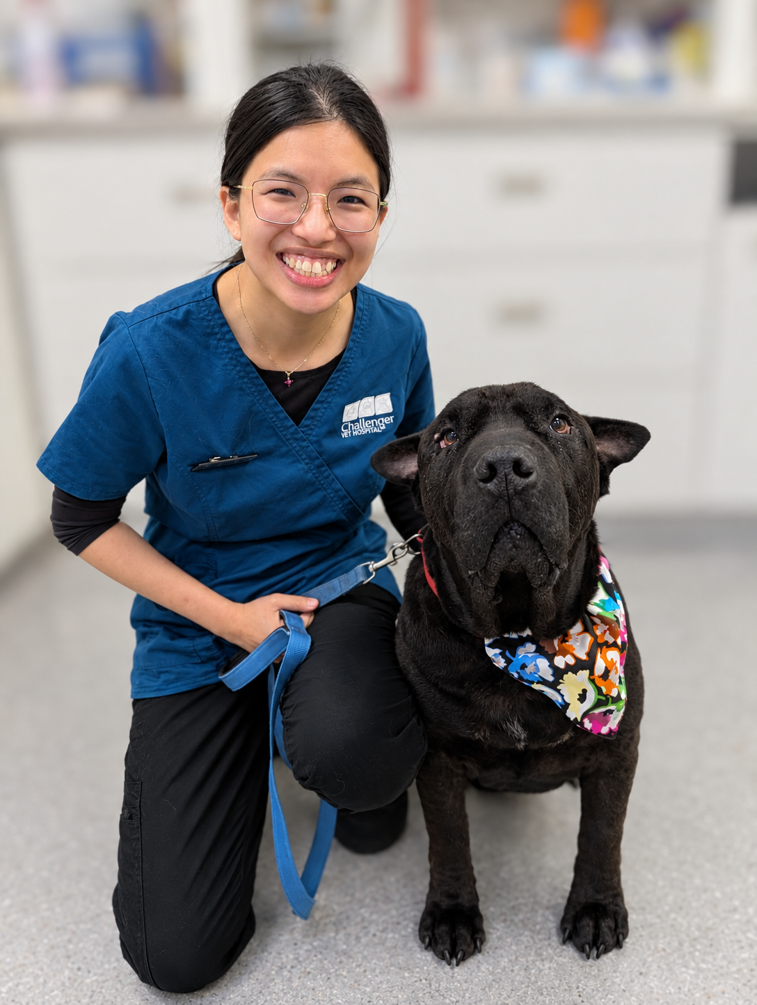 A smiling female veterinarian with a black dog wearing a bandanna.