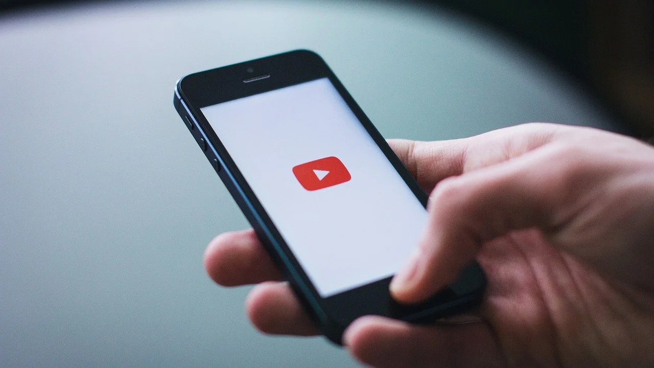 A person holding a smartphone displaying the YouTube logo on the screen.