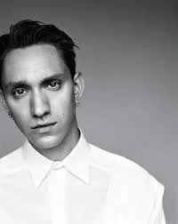 Black and white portrait of a young man with dark hair and a serious expression, wearing a white collared shirt