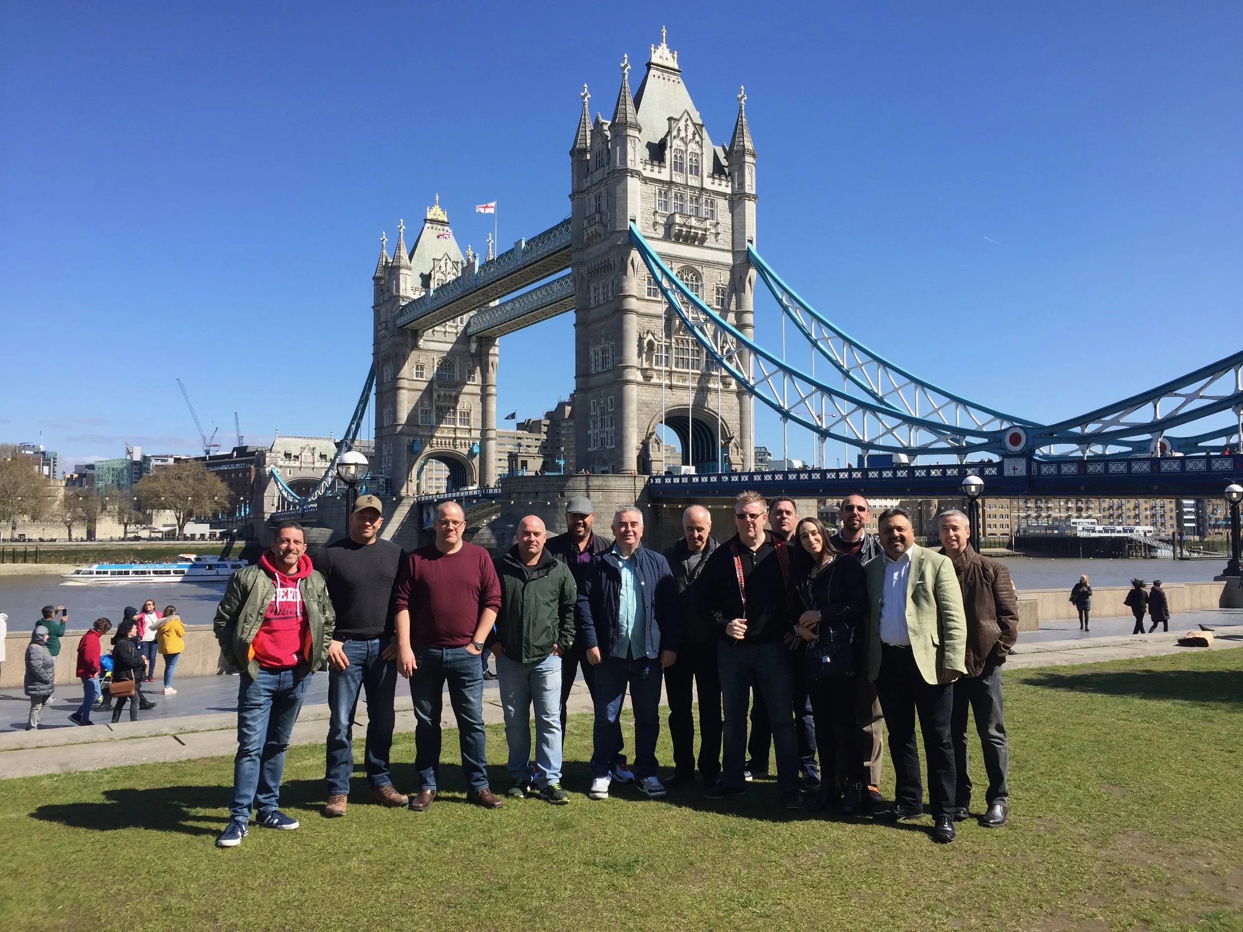 Group of people standing on grass with Tower Bridge and the River Thames in London, UK, in the background.