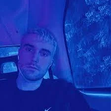 A young man with short blond hair taking a selfie inside a vehicle.