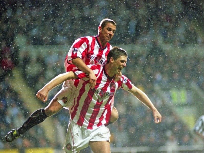 Two soccer players in red and white striped uniforms celebrating during a match in the rain.