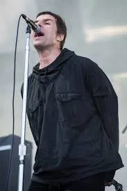 A person singing into a microphone on stage, wearing a black jacket.