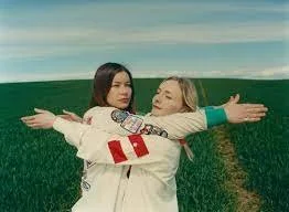 Two young women hugging in a green field with a clear sky