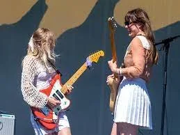 Two women, one young and one older, playing electric guitars together on stage during a live performance.