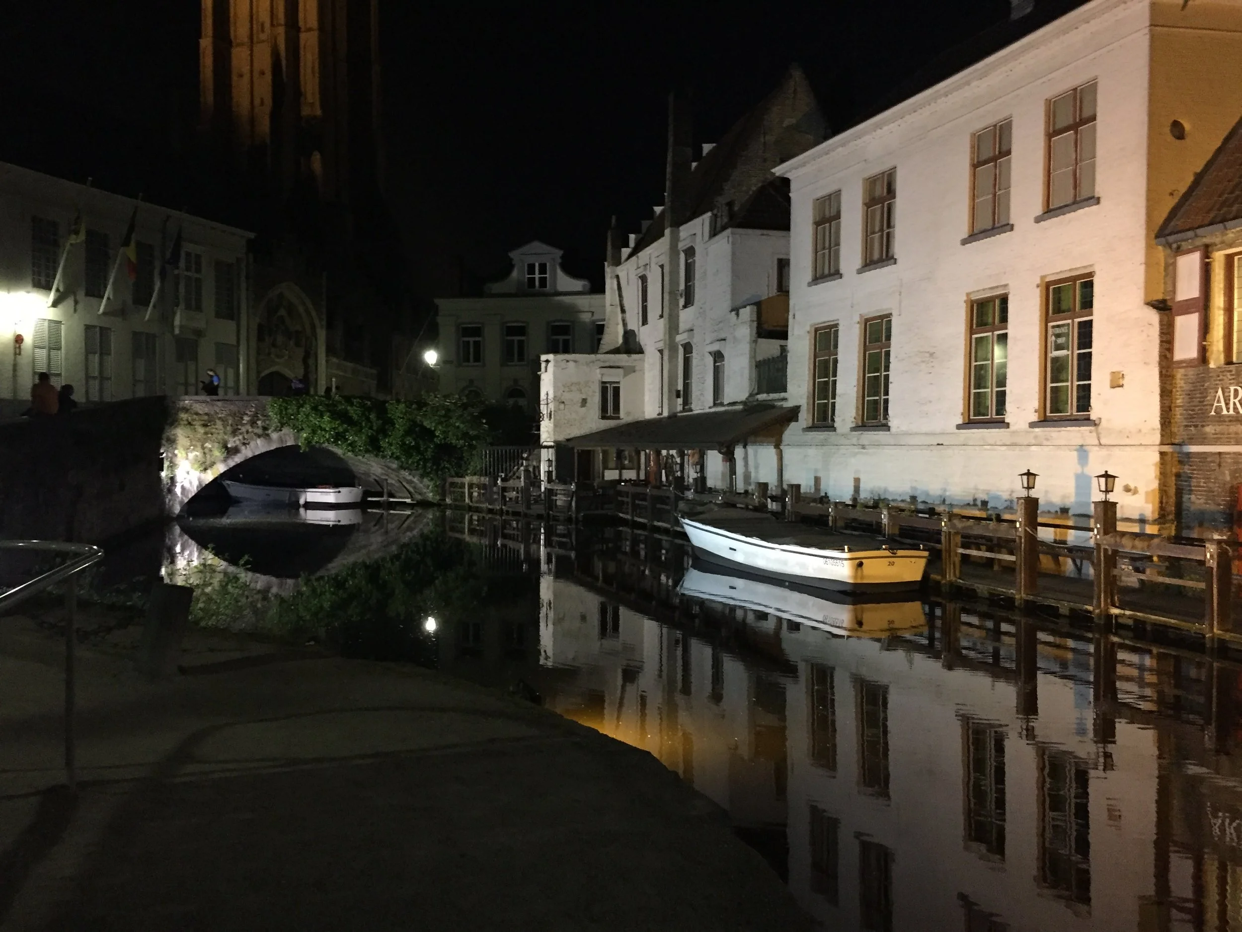 Night view of a canal with boats and historic buildings reflecting in the water, illuminated by streetlights.