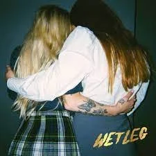 Two women hugging each other, one with long blonde hair and the other with long brown hair, in a close embrace