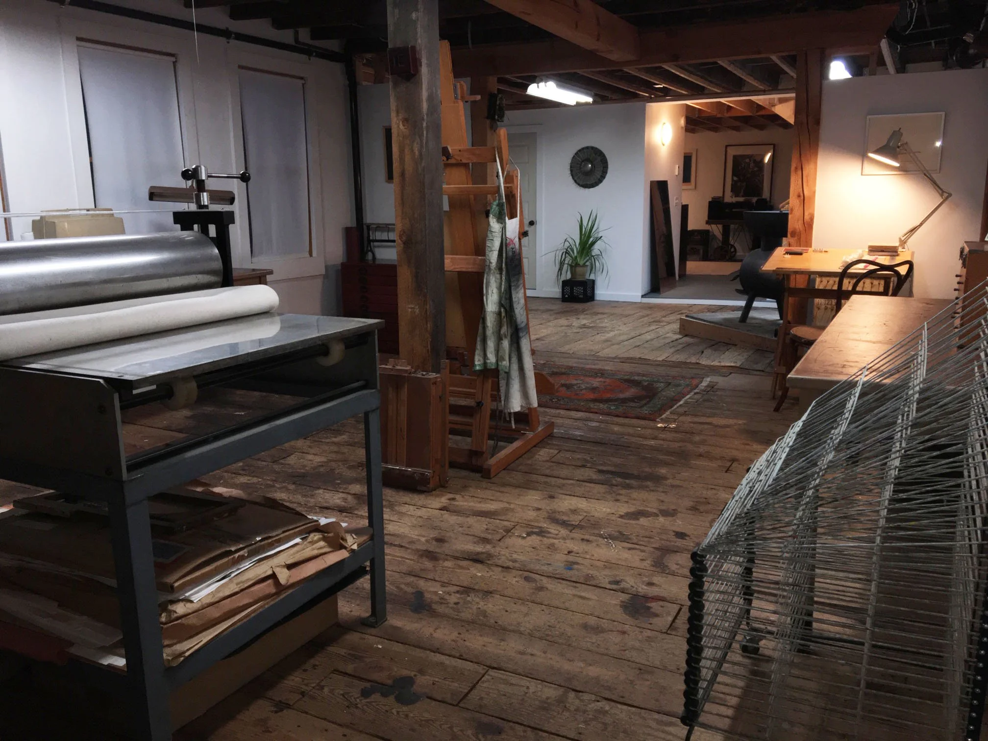 Photo of studio with etching press, drying racks, easel and workspace with light