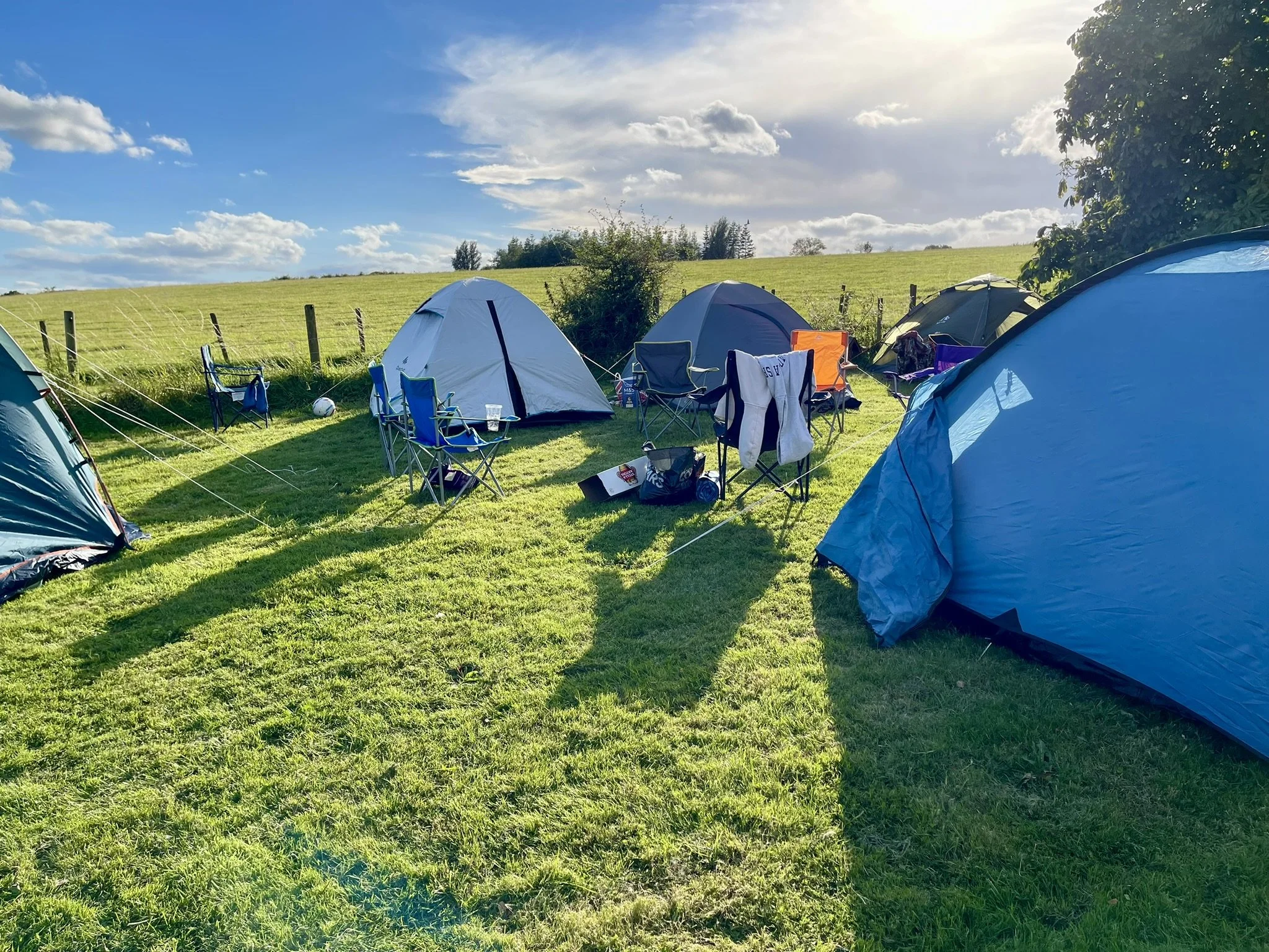 Tents and camping chairs set up in a grassy field under a blue sky.