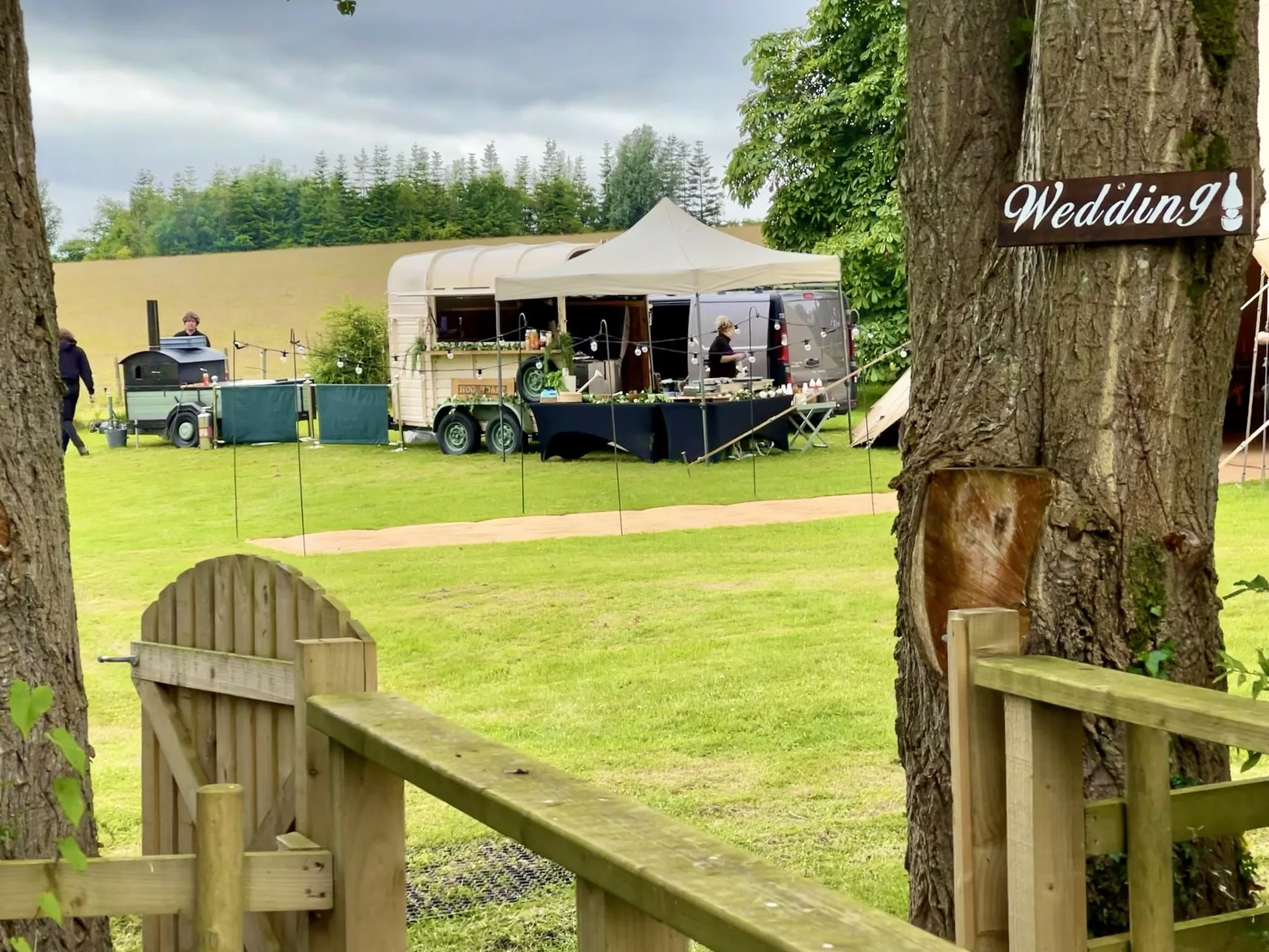 Outdoor wedding setup with a tent, food trailer, and sign on a tree.