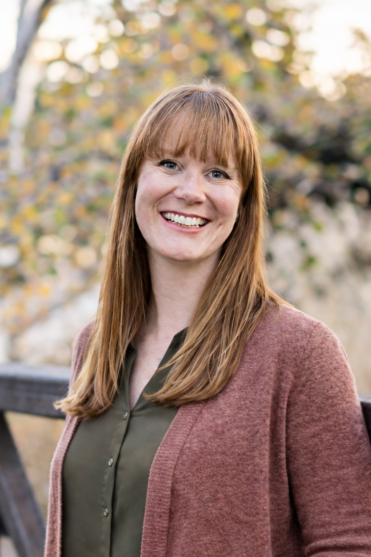 Smiling therapist standing outdoors by a wooden bridge, creating a warm and welcoming feeling for counseling and therapy services.