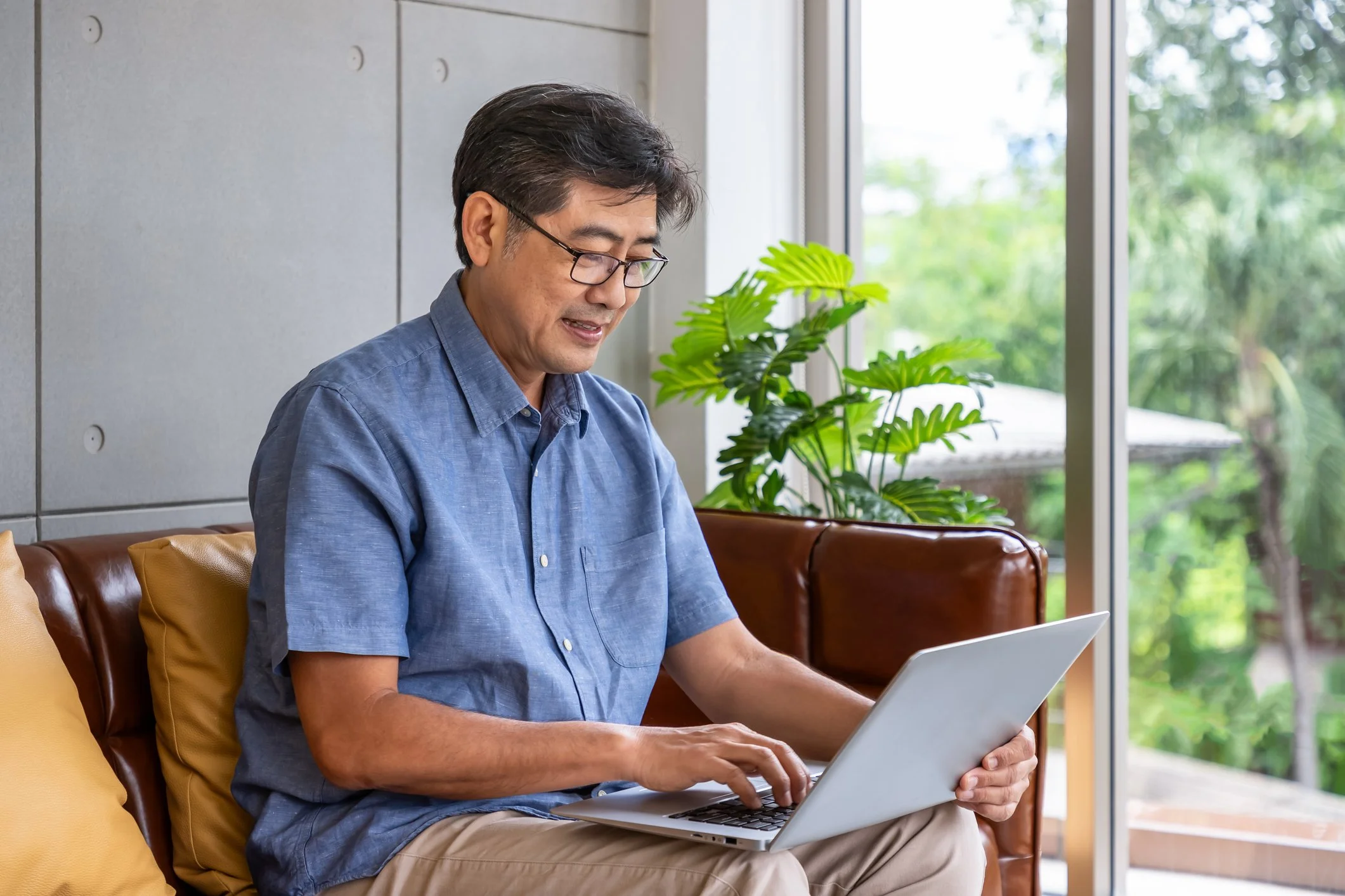 Older Asian man using a laptop at home, representing telehealth, online therapy, and convenient virtual support for older adults.