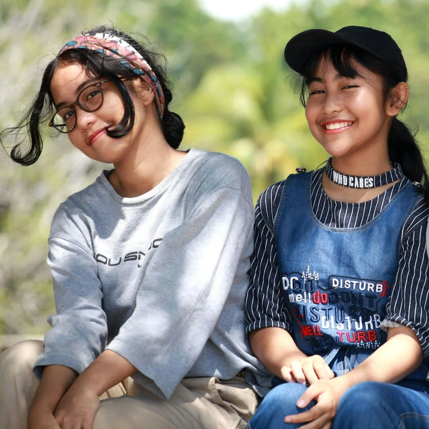 Two older children smiling and sitting in front of a forest.