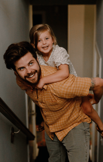 A man giving a young girl a piggyback ride, both of them smiling.