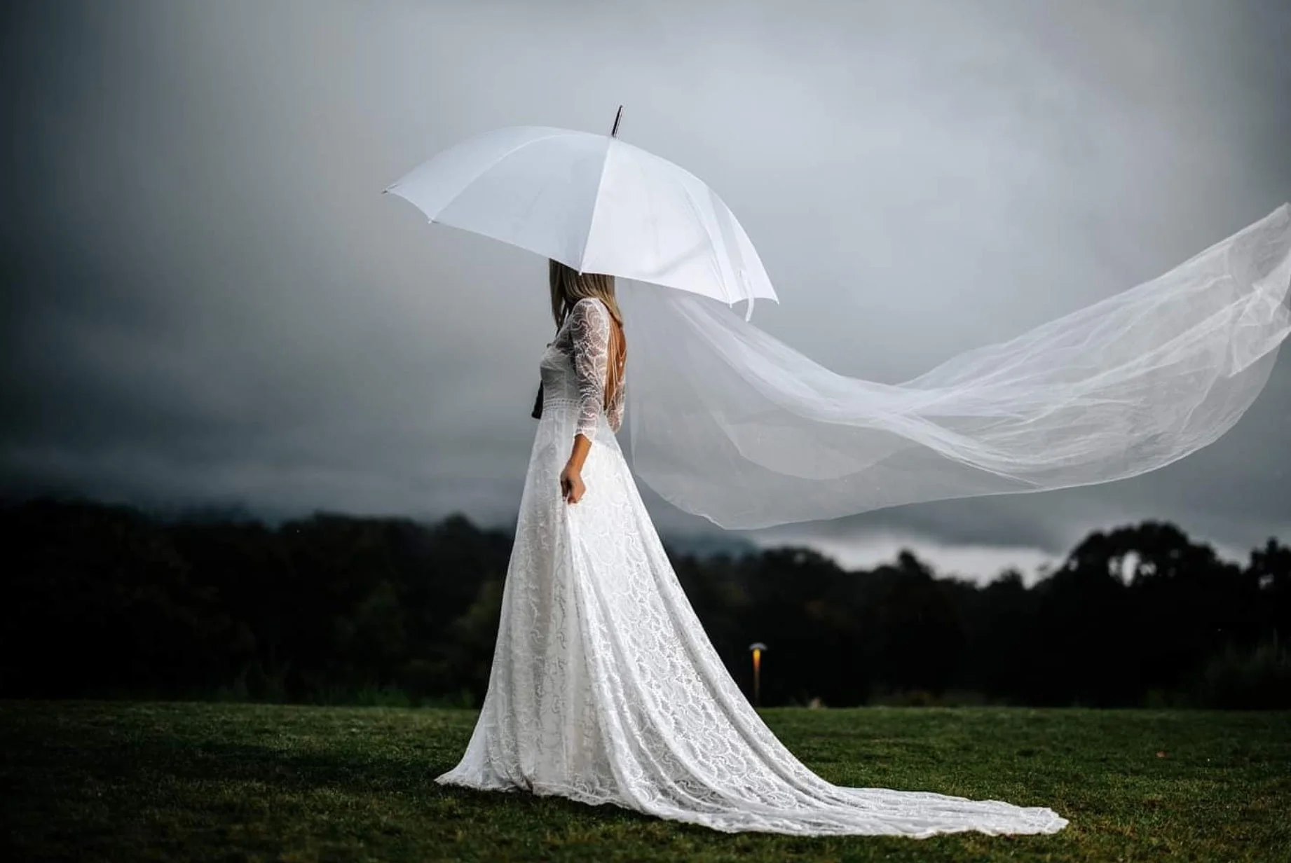 Bride standing under an umbrella with her wedding veil flowing in the wind