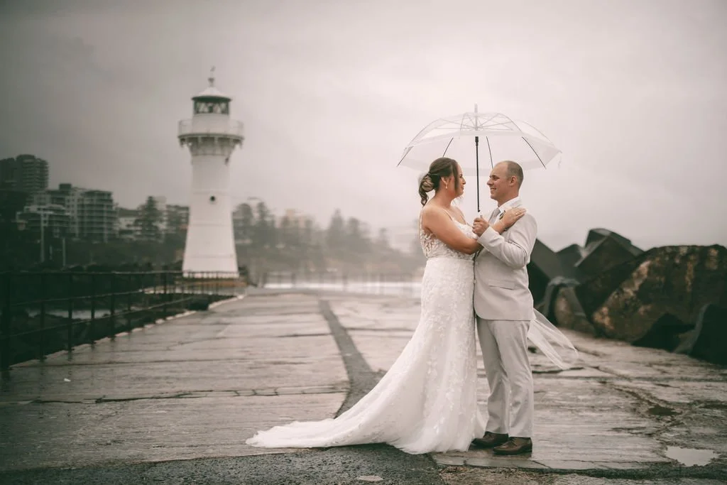 Maddison and Cody embracing beneath a clear umbrella near the lighthouse