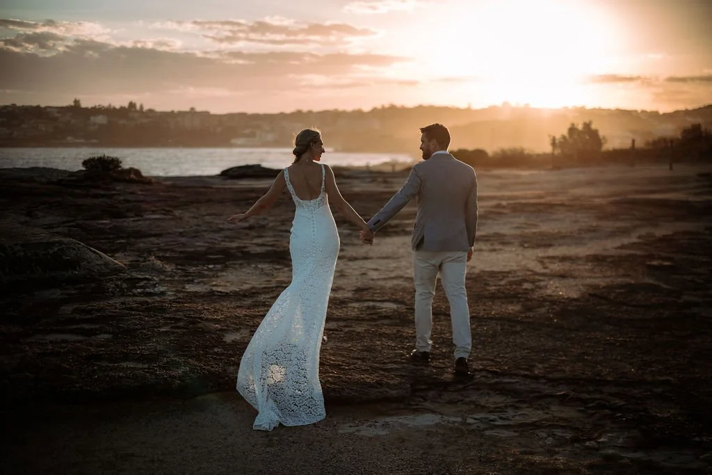 Erica and Chris walking hand in hand during sunset wedding portraits by the coast