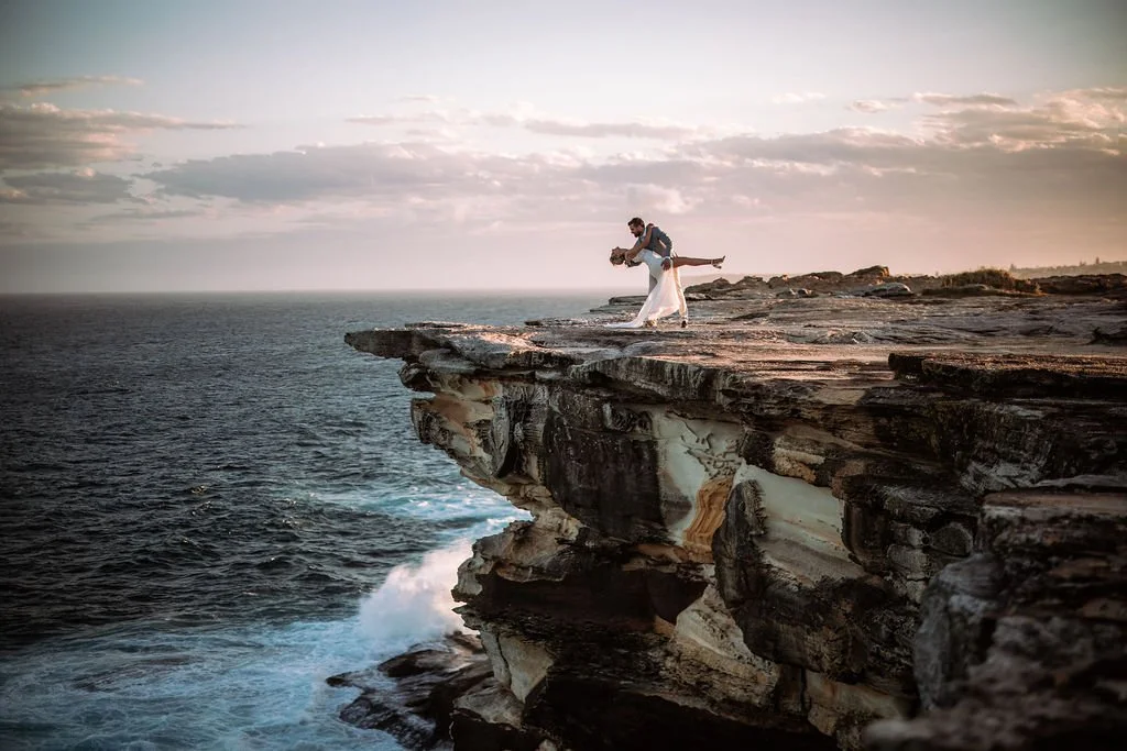 Erica and Chris embracing on a dramatic coastal cliff during their wedding photography session