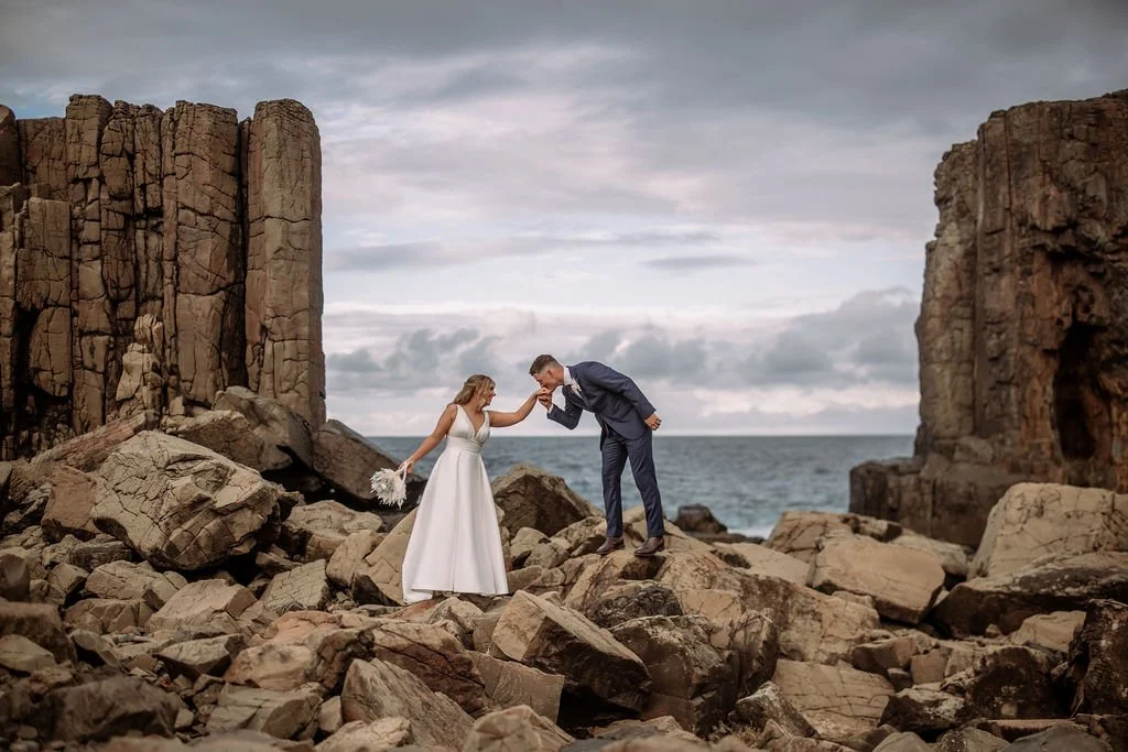 Charlotte and Ethan posing together among dramatic coastal rocks on their wedding day