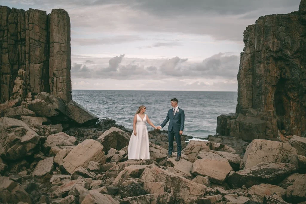 Charlotte and Ethan holding hands between dramatic coastal rock formations