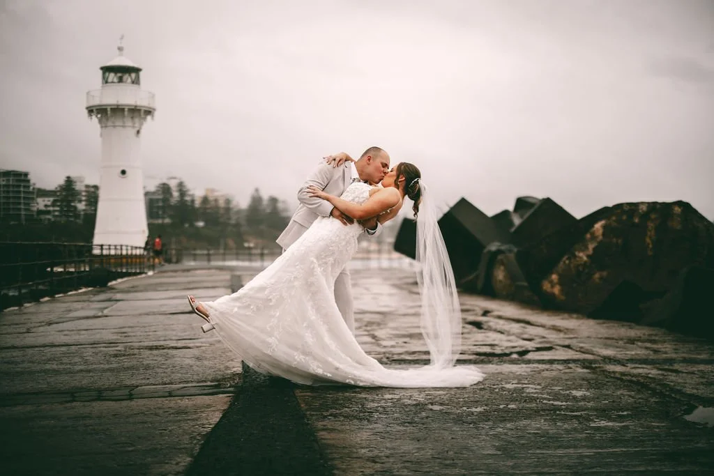 Maddison and Cody sharing a dip kiss during their wedding portraits by the lighthouse
