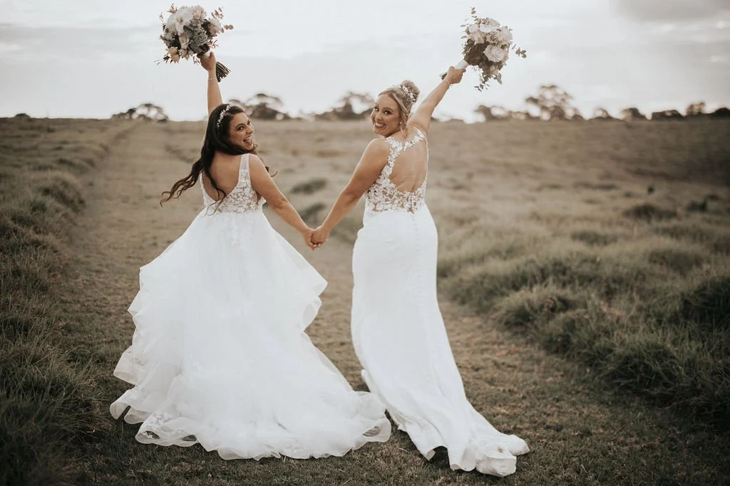Carla and Amie walking hand in hand with their wedding bouquets raised