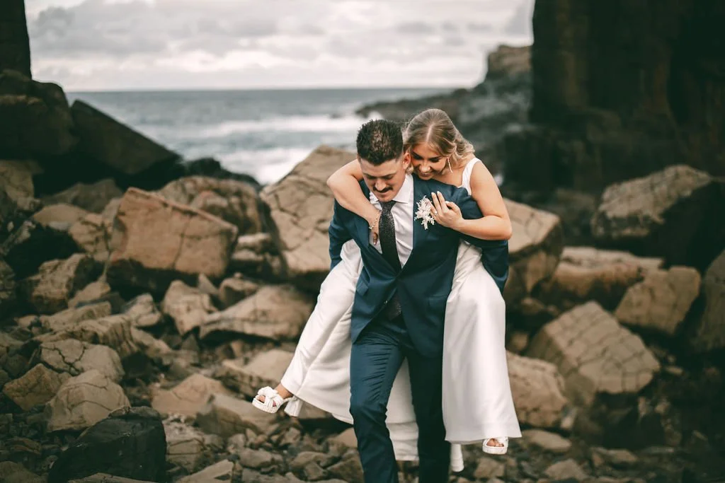 Ethan carrying Charlotte during playful wedding portraits on the rocky coastline