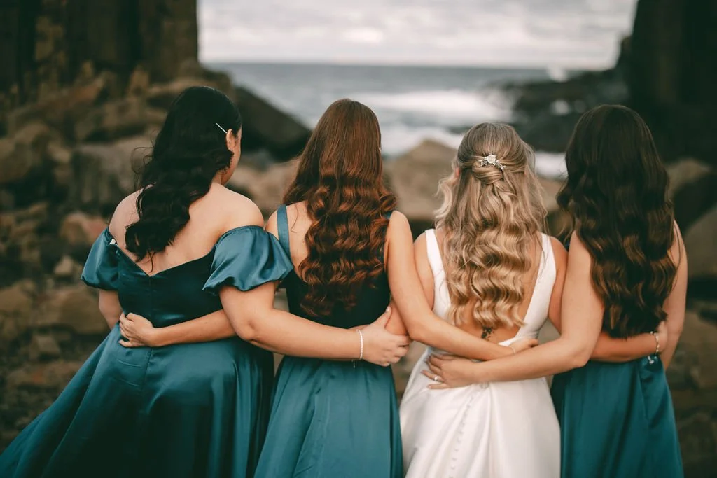 Charlotte standing arm in arm with her bridesmaids overlooking the coastline