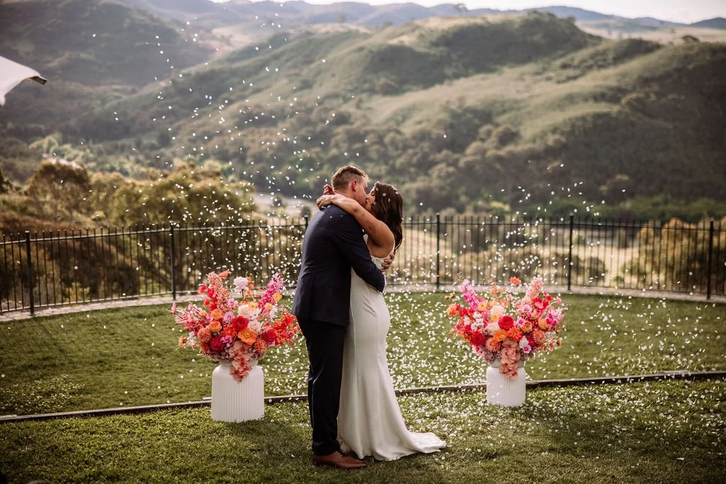 Bec and Luke embracing during their outdoor wedding ceremony with mountain views