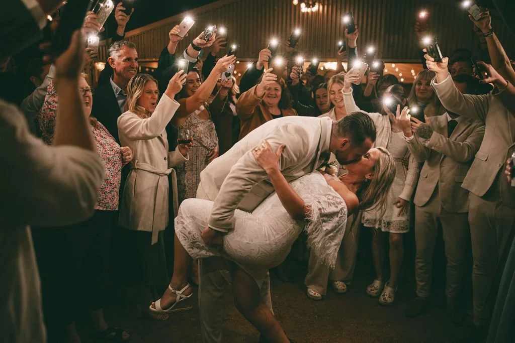 Corey dipping Allysha for a kiss surrounded by guests during their wedding reception