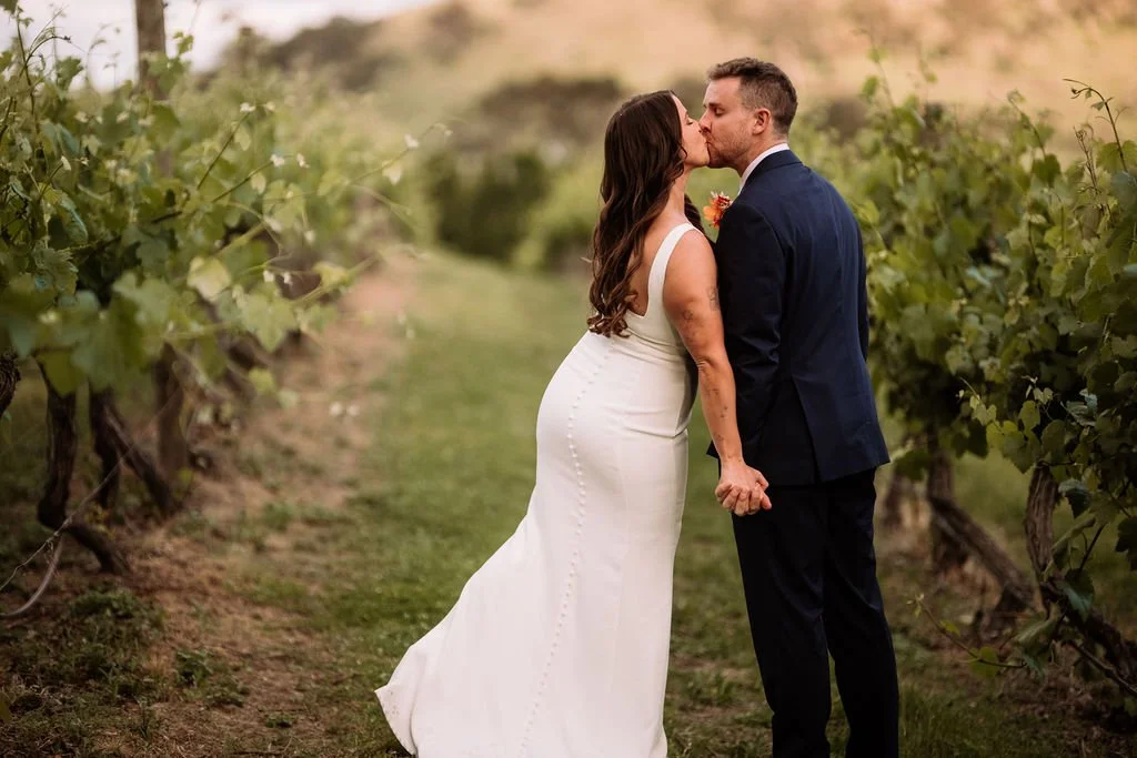 Bec and Luke kissing between vineyard rows on their wedding day