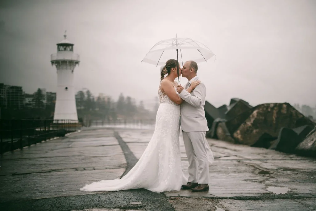 Maddison and Cody kissing beneath a clear umbrella during rainy wedding portraits