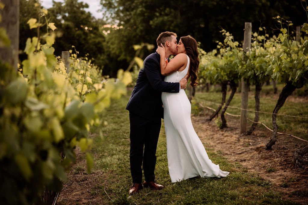 Bec and Luke kissing between vineyard rows during their wedding portraits