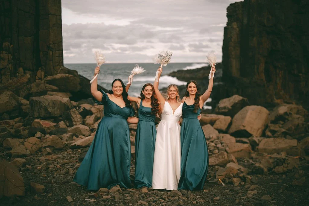 Charlotte celebrating with her bridesmaids in teal dresses during their coastal wedding portraits