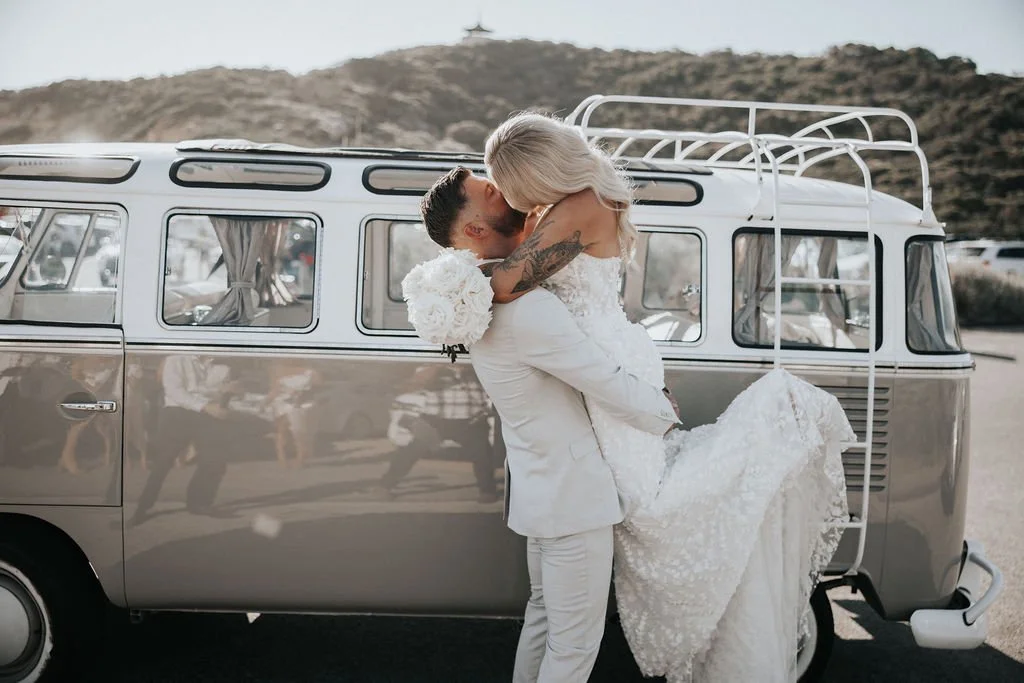 Blake dipping Miranda for a kiss beside their vintage wedding Kombi
