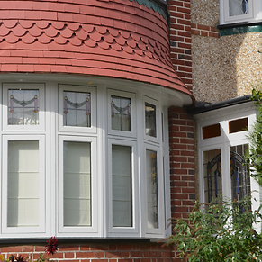 Close-up of a house with a red tiled bay window and a brick exterior, decorated with holiday garlands, and part of a white gutter and flush UPVC windows
