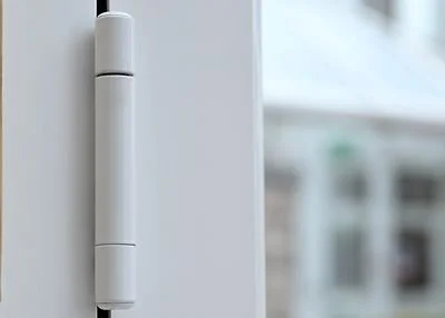 Close-up of a white door hinge or electronic device mounted on a white door or wall.