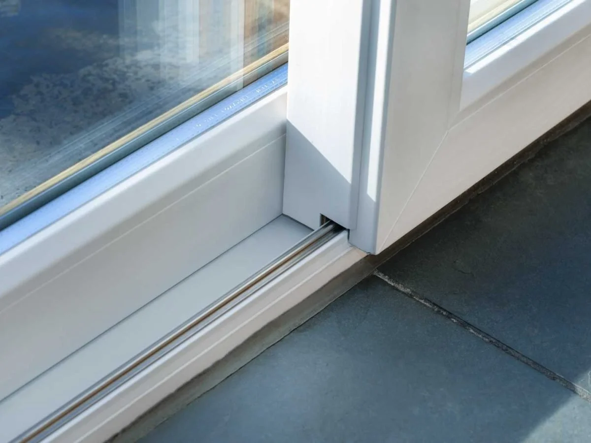 Close-up of a sliding glass door track and frame with a tiled floor.
