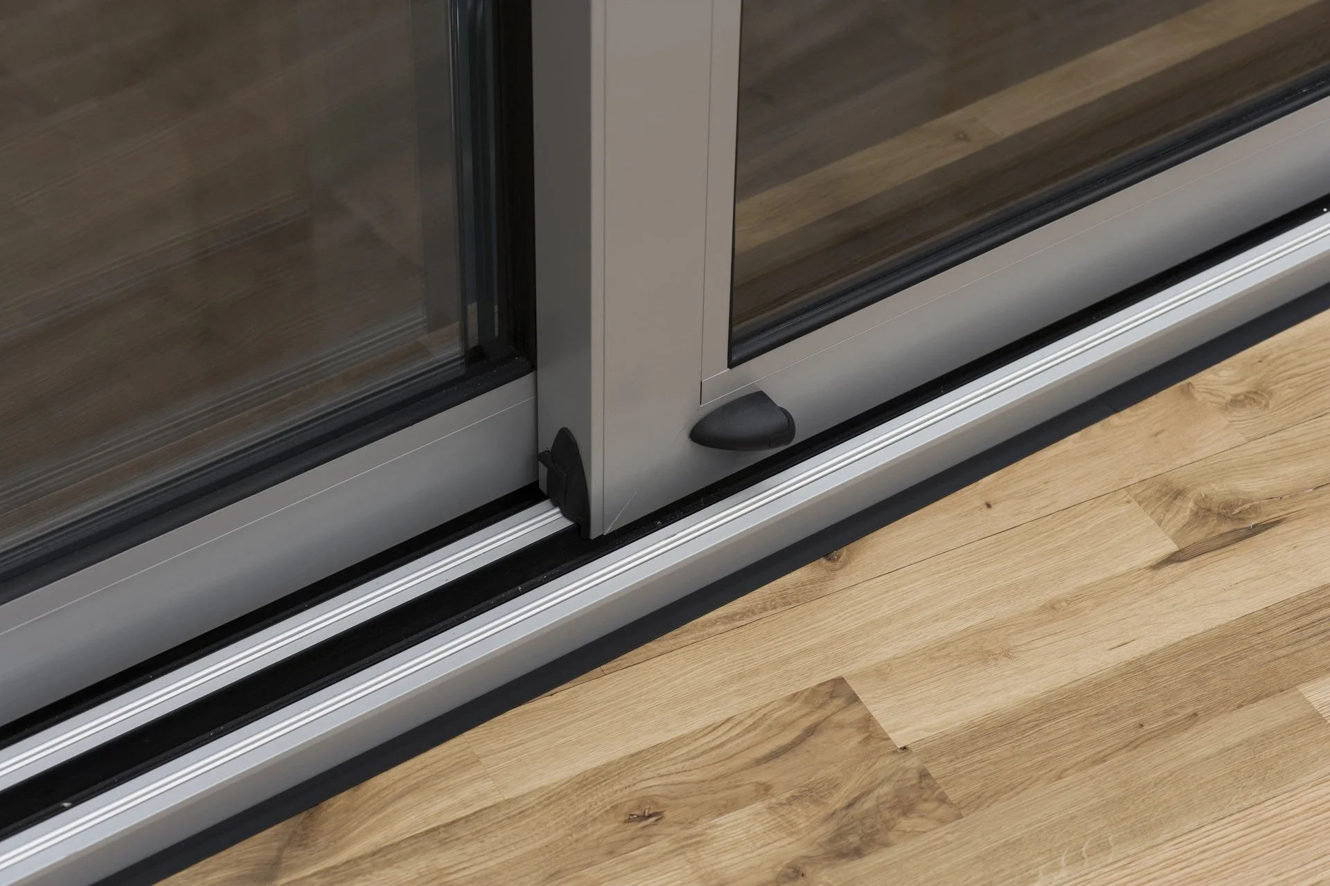 Close-up of sliding glass door track with a lock mechanism, metal frame, wooden floor, and part of the glass door.