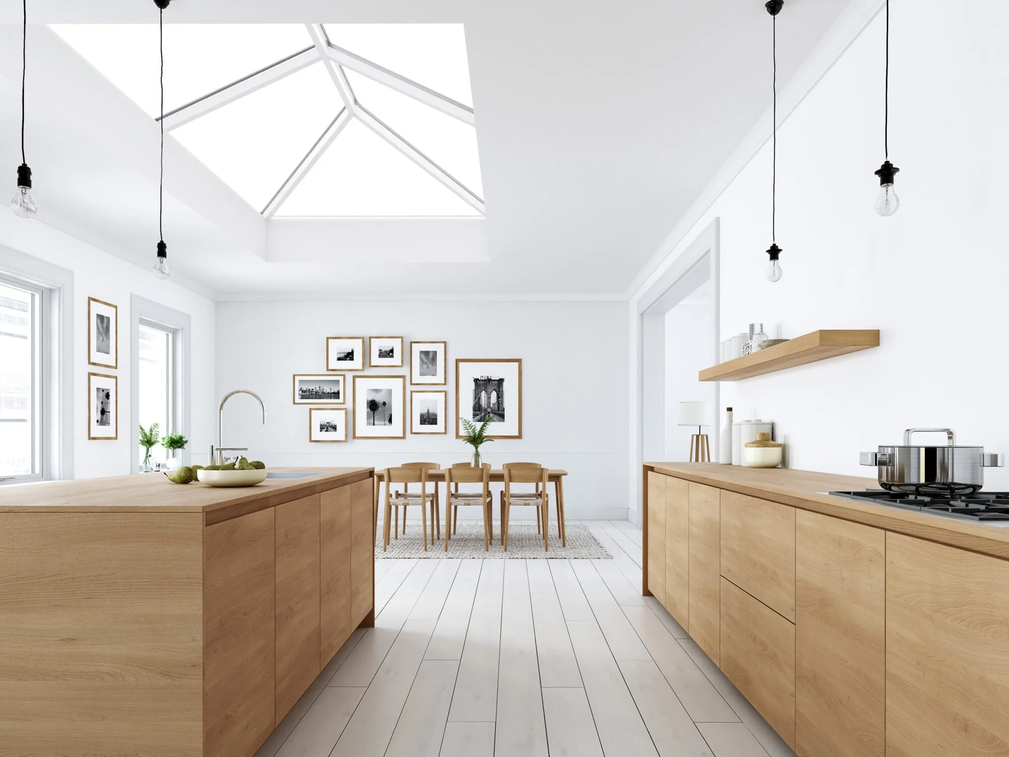Bright, minimalist kitchen with light wood cabinetry, high ceiling with skylight, pendant lights, and black-and-white framed photos on the wall.