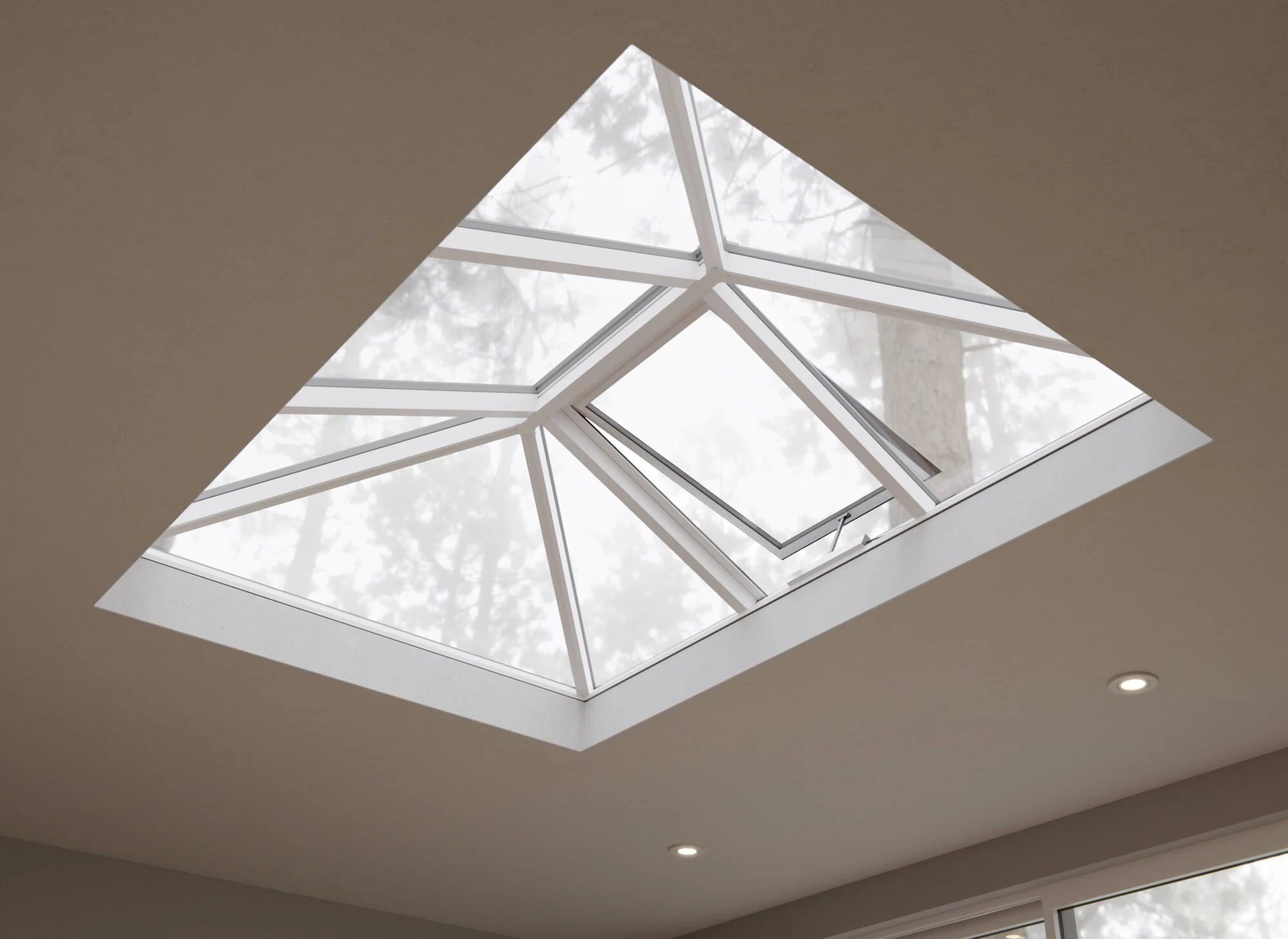 Indoor ceiling view of a skylight with multiple angles and clear glass panels, revealing trees outside.