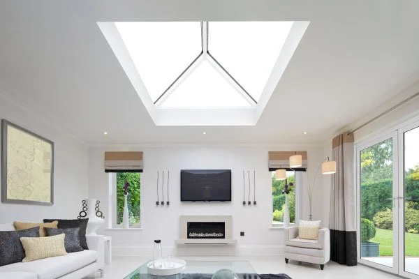 Bright living room with large skylight, white walls, modern furniture, a wall-mounted TV, and a view of a lush green outdoor garden.