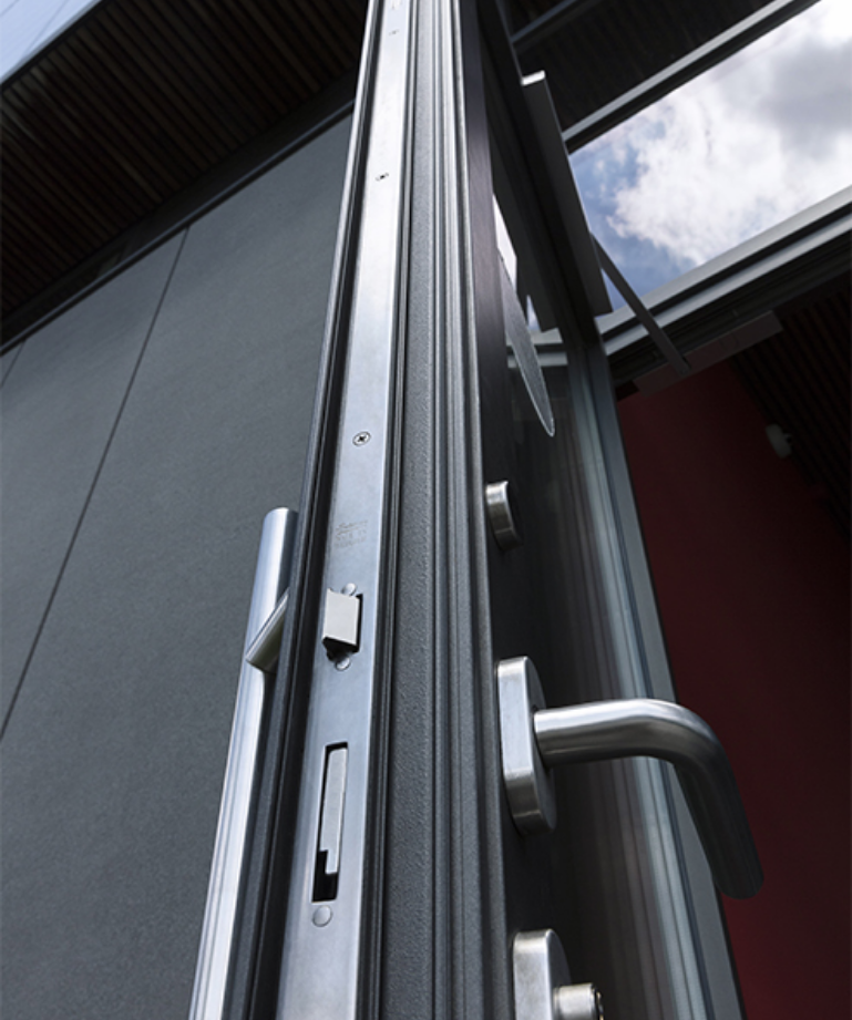 A close-up of a modern metal door lock and handle on an exterior door, with a window showing a cloudy sky.