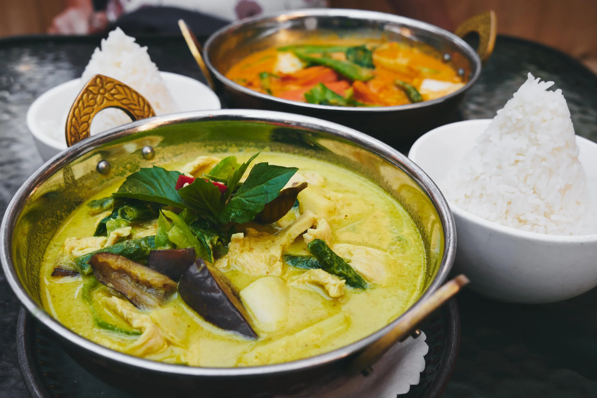 Thai curry dishes with rice and vegetable garnishes.