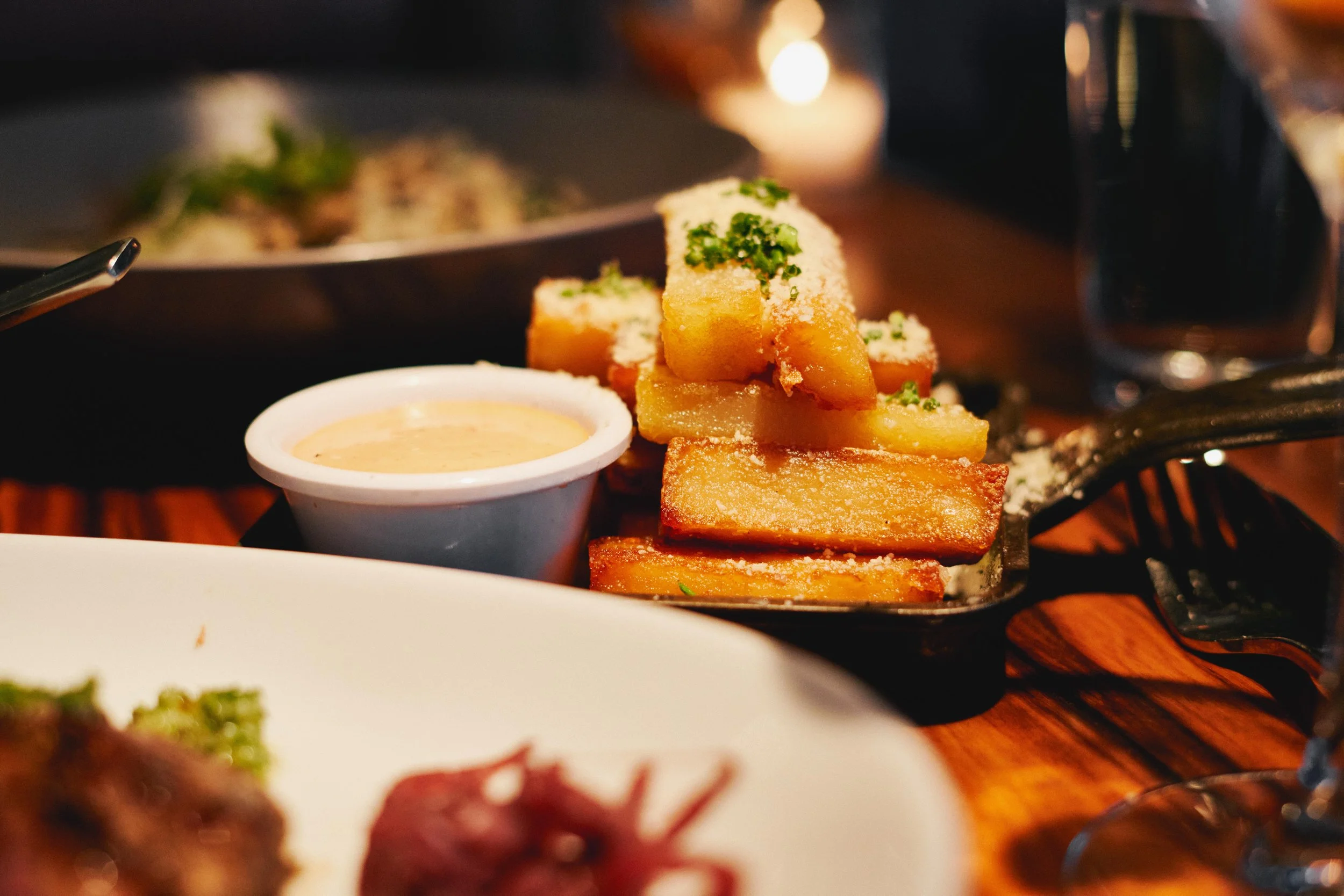 Fried food items topped with green herbs, served with a small cup of dipping sauce on a wooden table.